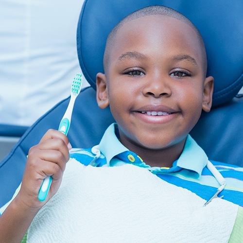 A young boy wearing a striped shirt holds a manual toothbrush and smiles