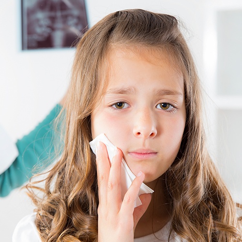 Little girl holding cold compress to check during emergency dentistry visit