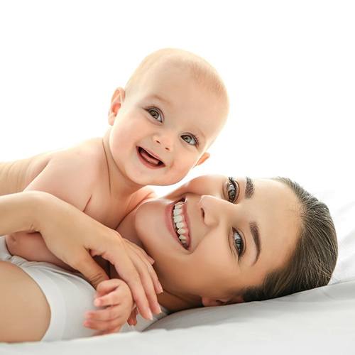 A mother and baby smiling while laying on a bed 