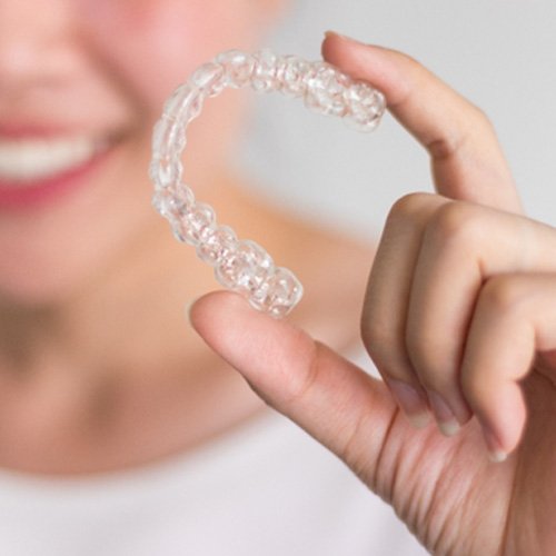 Teen girl smiling while holding Invisalign aligner