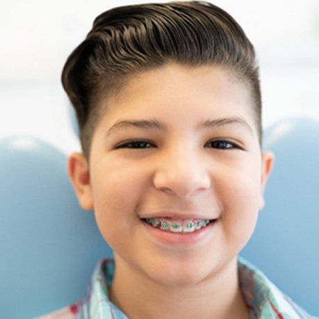 Child with traditional braces smiling in treatment chair