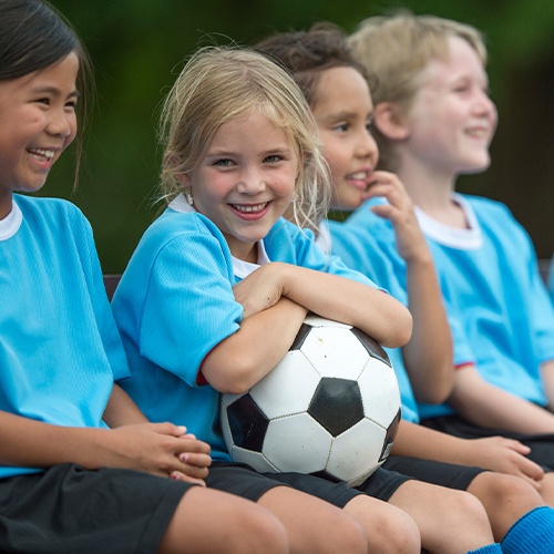 Little girl holding soccer ball with healthy smile after silver diamine fluoride treatment