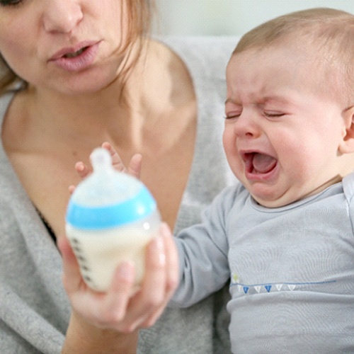 A mother attempting to give her baby a bottle, but the child is crying