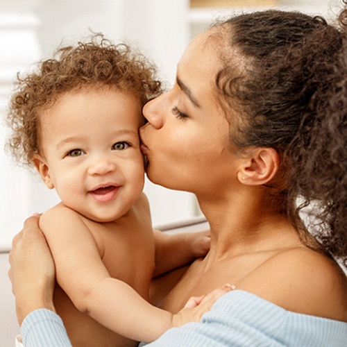 A mother holding and kissing her baby who appears happy 