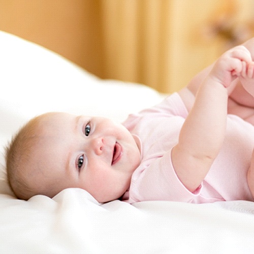 A baby lying on its back on a bed and playing with its toes