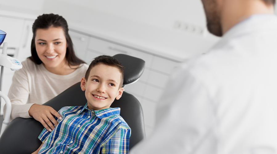 Dentist talking to young boy and his mom in dental exam room