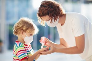 mom giving hand sanitizer to child, both wearing face masks