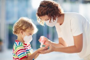 mom giving hand sanitizer to child, both wearing face masks 