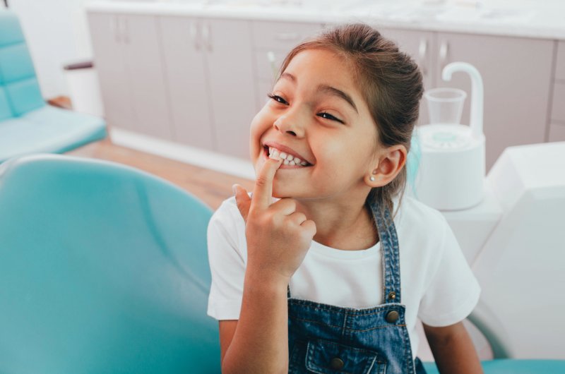 Child smiling and pointing to her teeth at dentist appointment