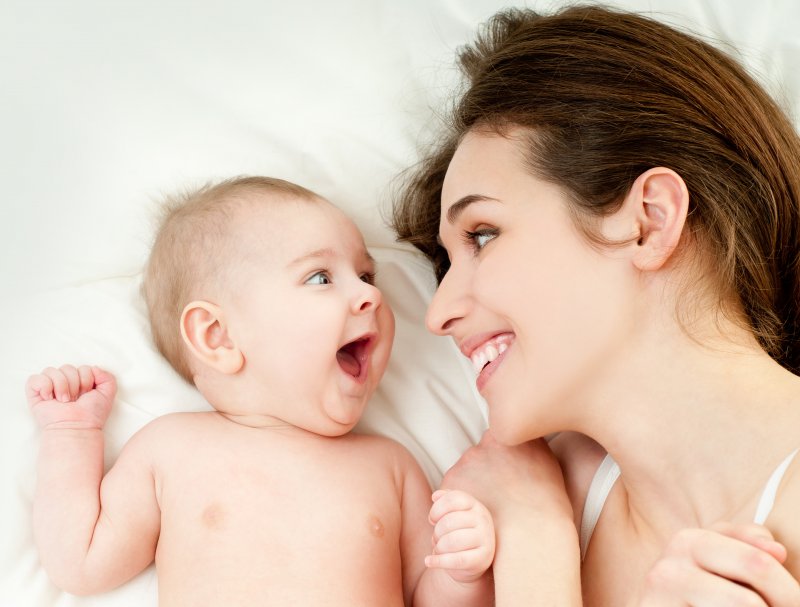 a mother and her baby smile at each other while laying on a bed
