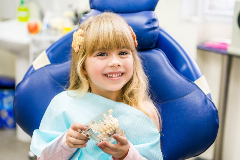 a little girl smiling while holding a mouth mold and seeing her pediatric dentist in Levittown