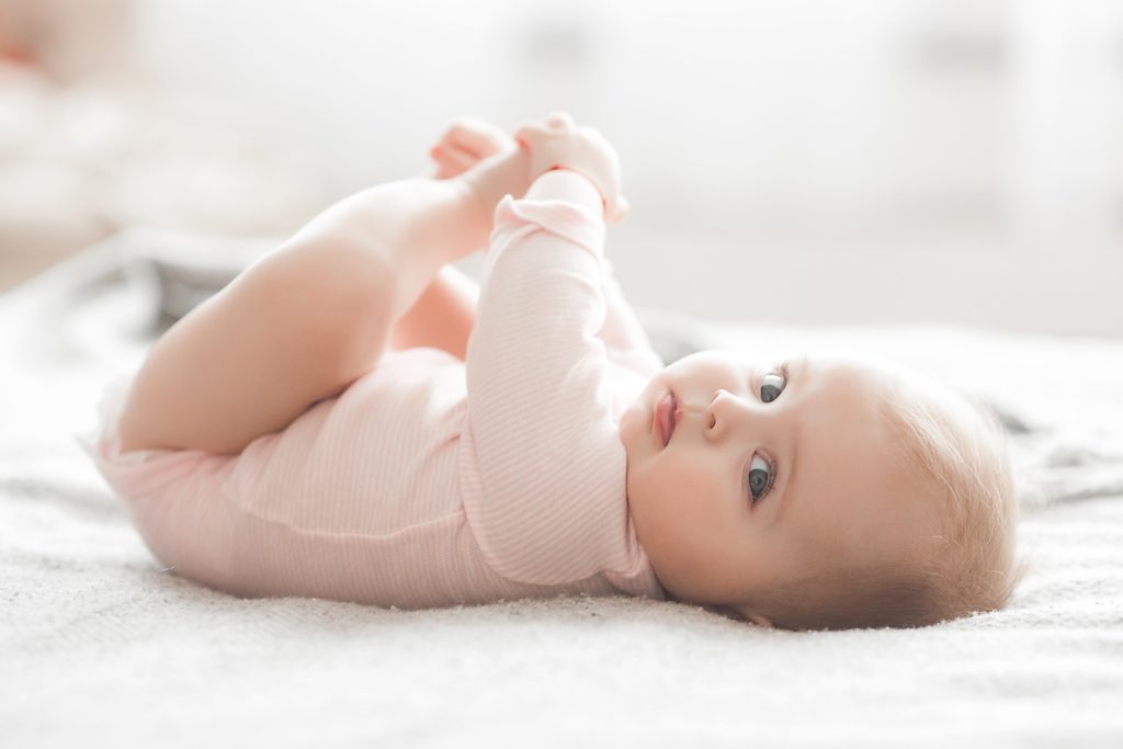 Baby holding their feet while lying on soft blanket